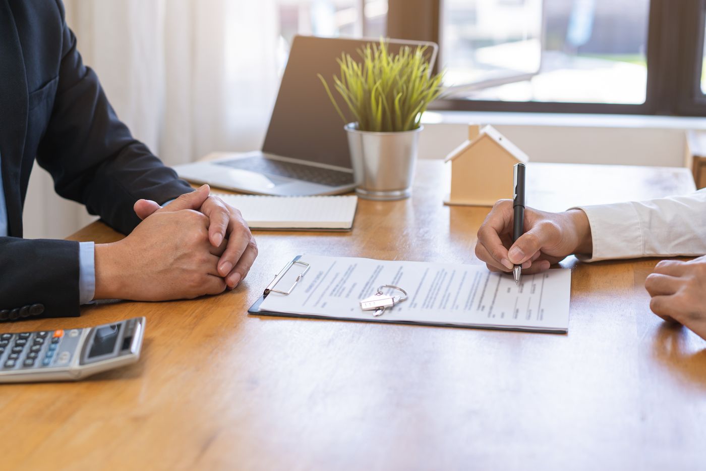 Buyer signing loan closing documents with a house model and keys on the table